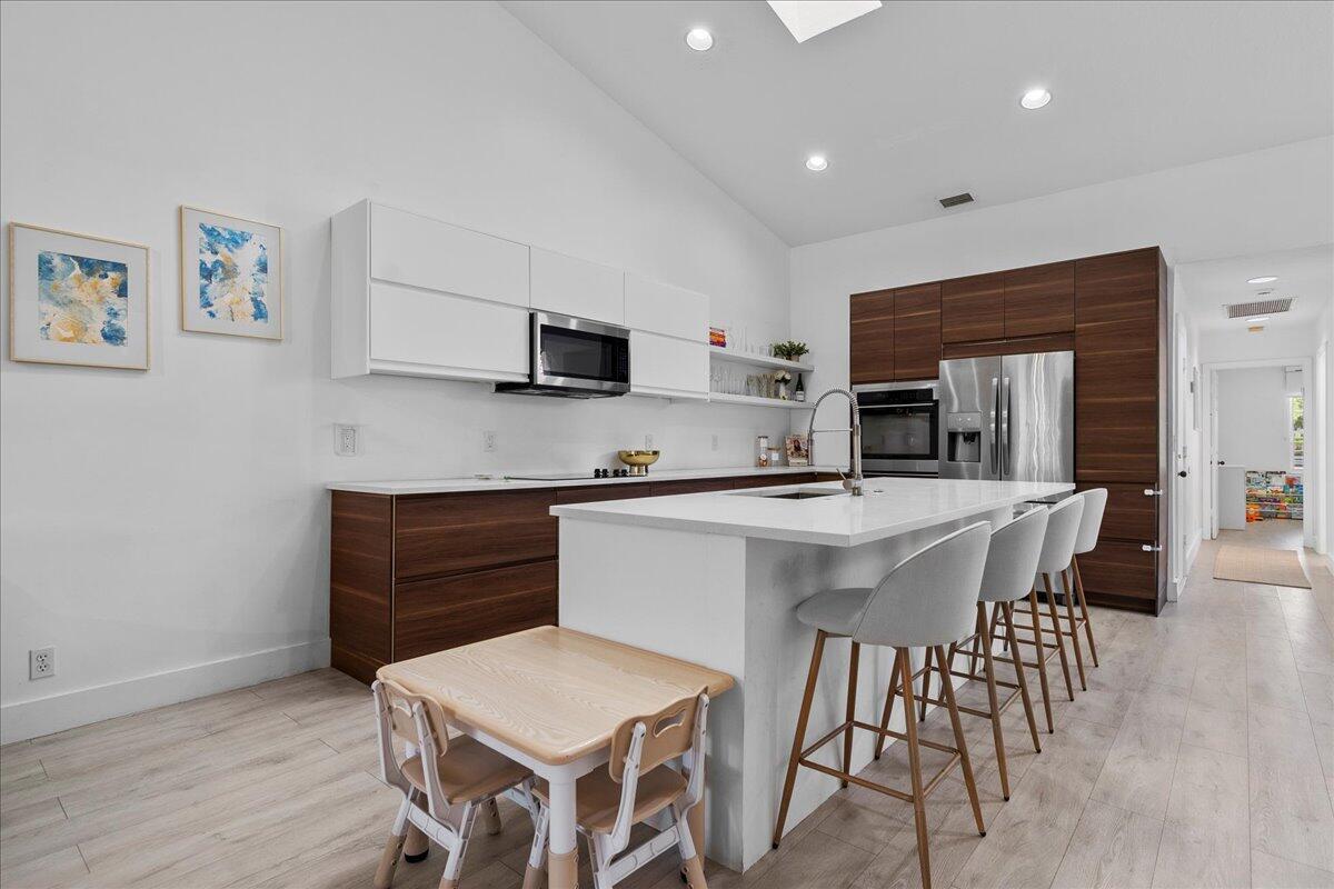 A modern kitchen features white upper cabinets, wood-toned lower cabinets, a central island, and barstools — 8304 Vía Di Veneto, Boca Raton FL 33496, BOCA RATON, FL