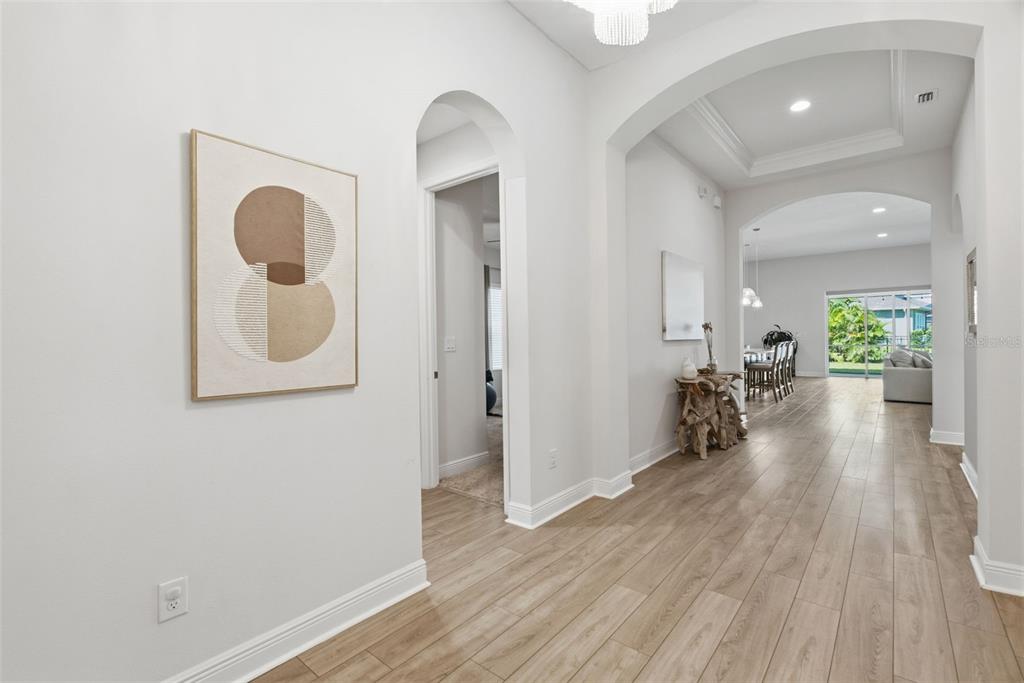 A bright hallway with light wood-look flooring leads to an open living area with arches — 5604 WAYFARER AVENUE, APOLLO BEACH, FL