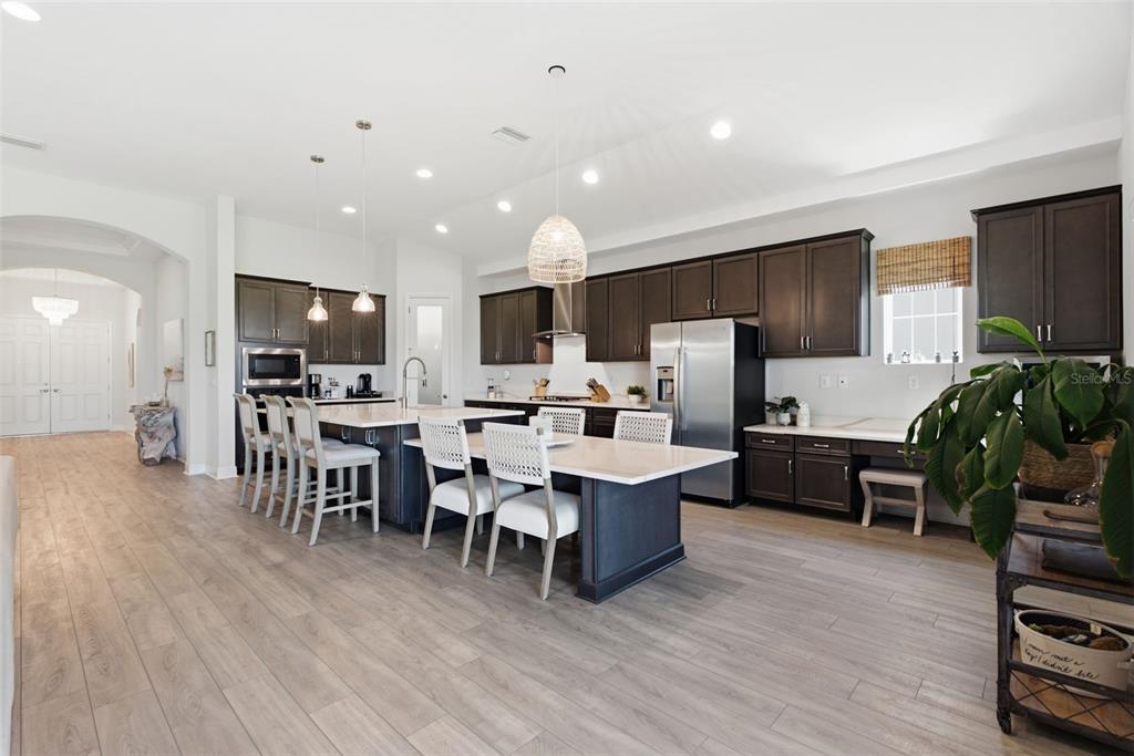 A modern kitchen features dark cabinetry, a large island with seating, and light wood flooring — 5604 WAYFARER AVENUE, APOLLO BEACH, FL