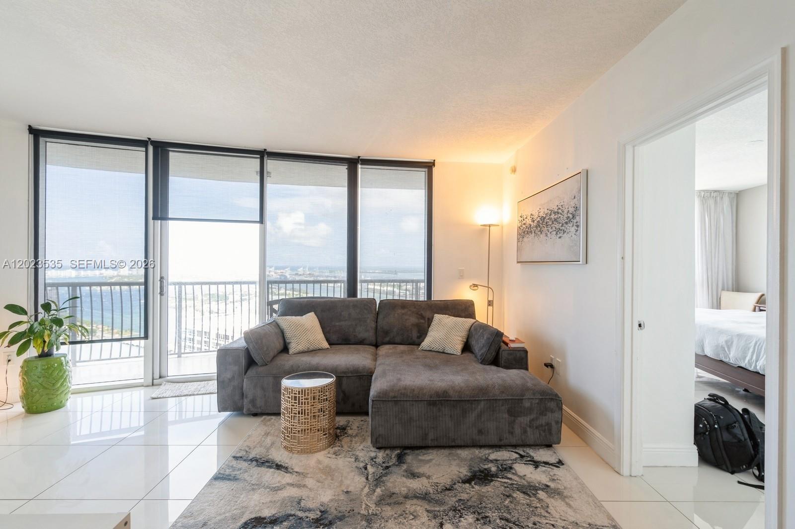 A living room features a grey sectional sofa, a patterned rug, and floor-to-ceiling windows — 1750 N Bayshore Dr # 4702, Miami FL 33132, MIAMI, FL