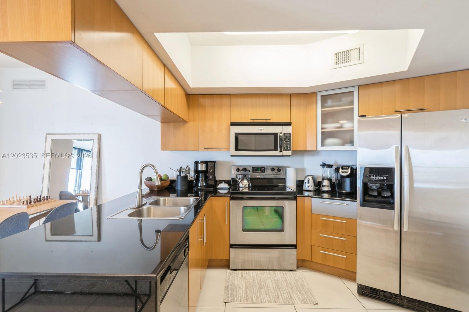 A kitchen features light wood cabinets, stainless steel appliances, and black countertops — 1750 N Bayshore Dr # 4702, Miami FL 33132, MIAMI, FL