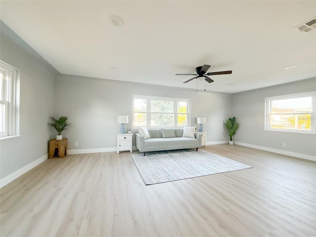 A spacious living room features light-colored wood flooring, gray walls, and a central sofa — 13290 3RD STREET E, MADEIRA BEACH, FL