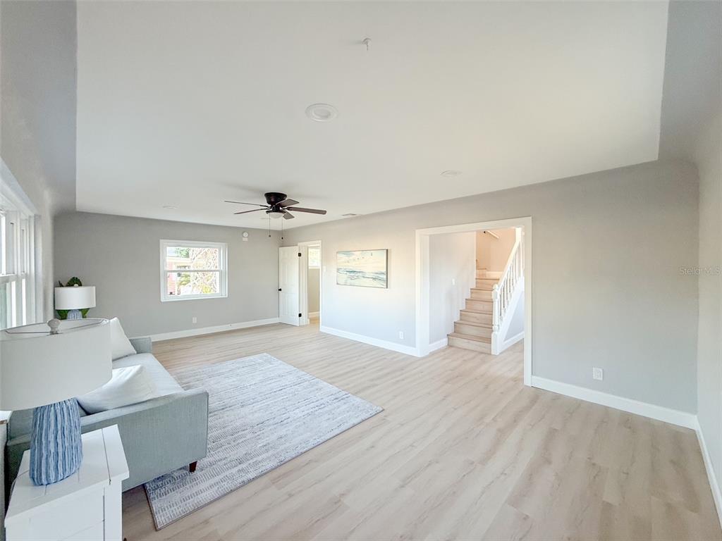 A living room with light wood floors, a ceiling fan, and a staircase in view — 13290 3RD STREET E, MADEIRA BEACH, FL
