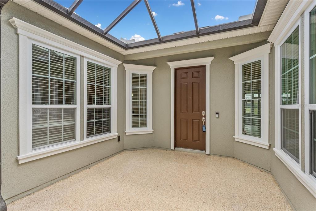 A covered patio features a brown door, multiple windows with white trim, and a textured floor — 124 BALMY COAST ROAD, GROVELAND, FL