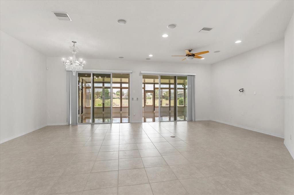 A spacious, white-walled living room features tile flooring, a crystal chandelier, and sliding glass doors — 124 BALMY COAST ROAD, GROVELAND, FL