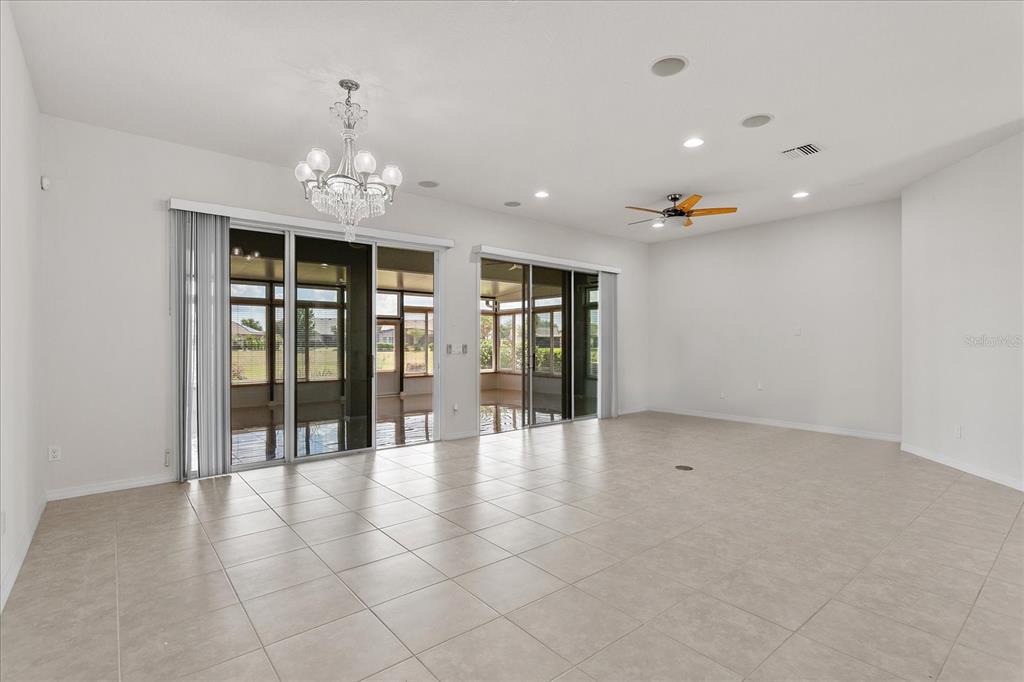 A spacious, tiled living room features a crystal chandelier, ceiling fan, and large sliding glass doors — 124 BALMY COAST ROAD, GROVELAND, FL