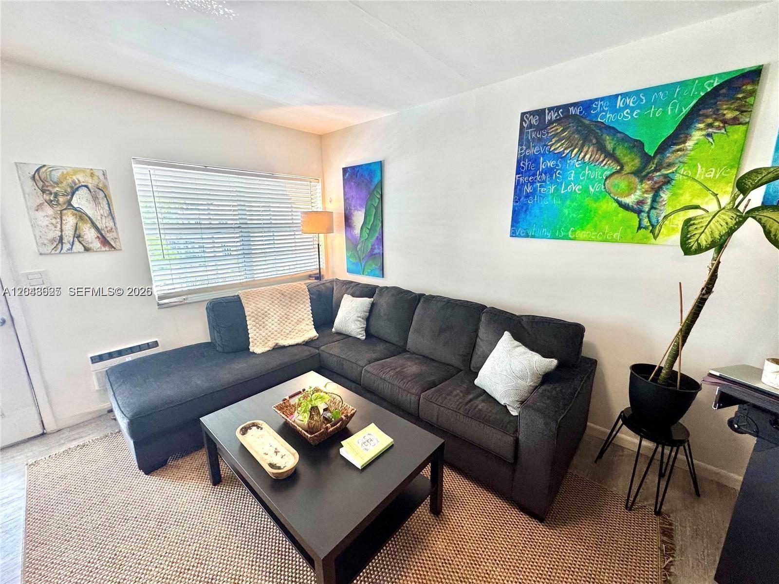 A living room features a dark sectional sofa, a coffee table, and colorful wall art — 330 74th St # 15, Miami Beach FL 33141, MIAMI BEACH, FL