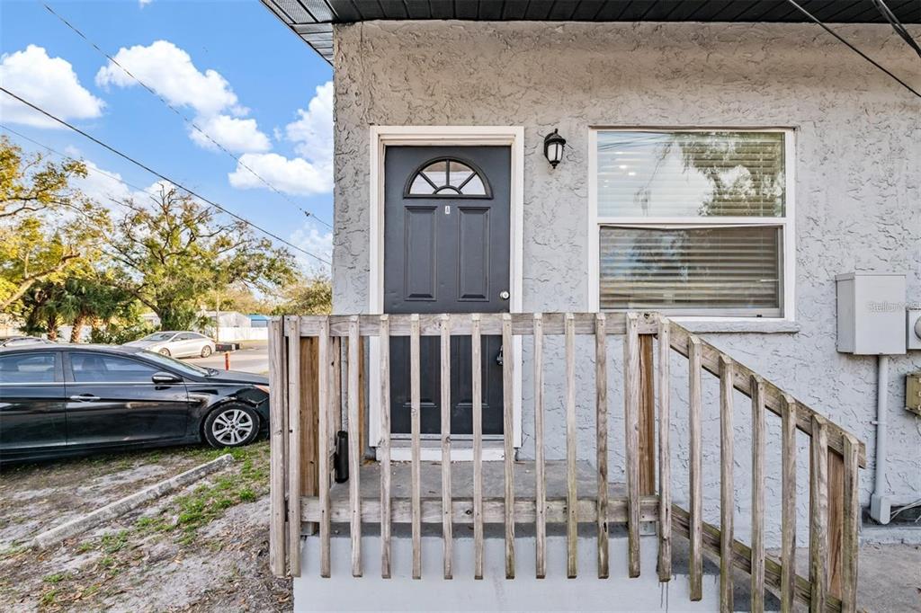 An exterior view of a building entrance with a wooden porch railing and dark door — 8304 N 13TH STREET, TAMPA, FL