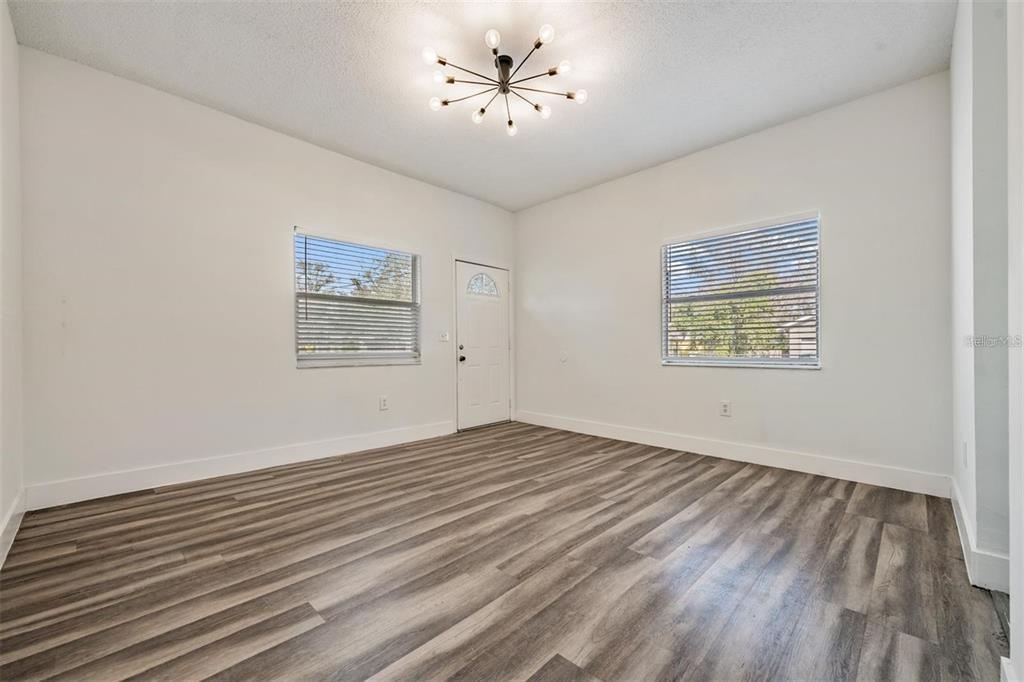 An empty room features white walls, wood-look flooring, two windows with blinds, and a ceiling light — 8304 N 13TH STREET, TAMPA, FL