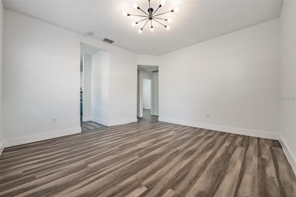 A bright, empty room features white walls, wood-look flooring, and a modern sputnik chandelier — 8304 N 13TH STREET, TAMPA, FL