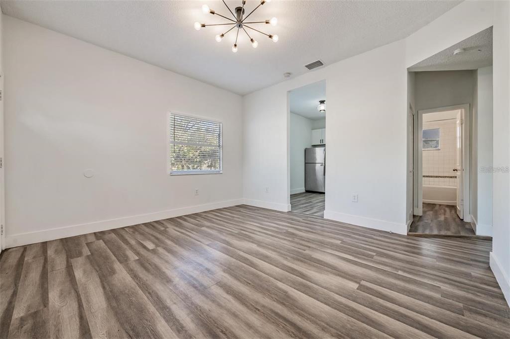 An empty room with light-colored walls, wood-look flooring, a modern chandelier, and an adjacent kitchen — 8304 N 13TH STREET, TAMPA, FL