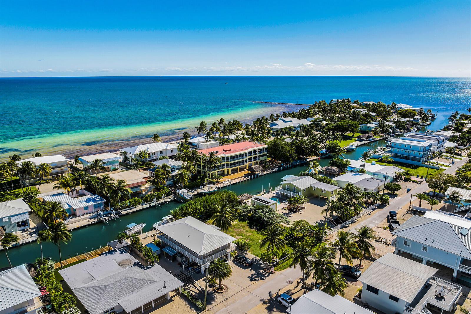 An aerial view shows waterfront homes, a canal, and a multi-story building near the ocean — 149 Iroquois Drive, Islamorada FL 33036, ISLAMORADA, FL