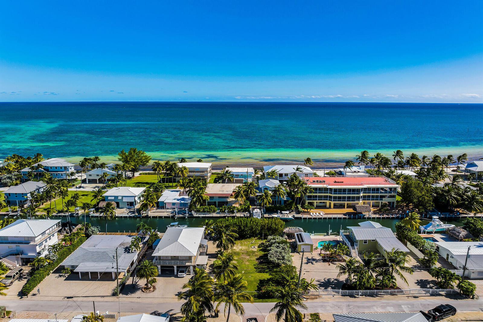 An aerial view shows waterfront homes and a multi-story building along a canal near the ocean — 149 Iroquois Drive, Islamorada FL 33036, ISLAMORADA, FL
