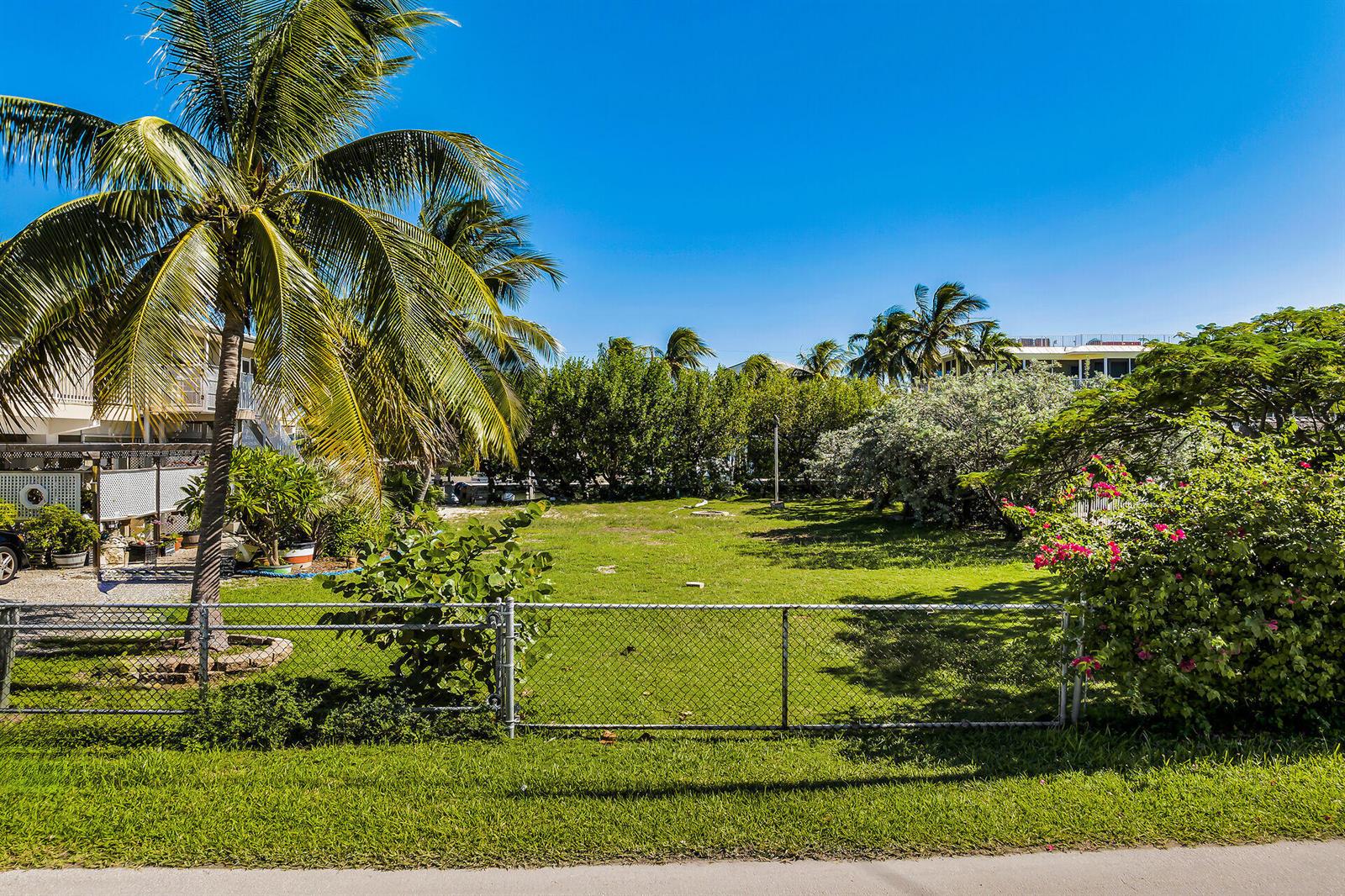 A fenced, grassy vacant lot is surrounded by palm trees and lush tropical vegetation — 149 Iroquois Drive, Islamorada FL 33036, ISLAMORADA, FL