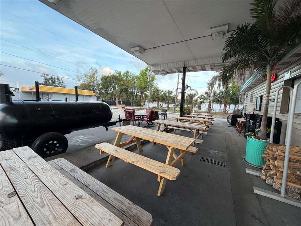 An outdoor patio area features wooden picnic tables, a large black smoker, and a palm tree — 1095 US HIGHWAY 17 S, BARTOW, FL