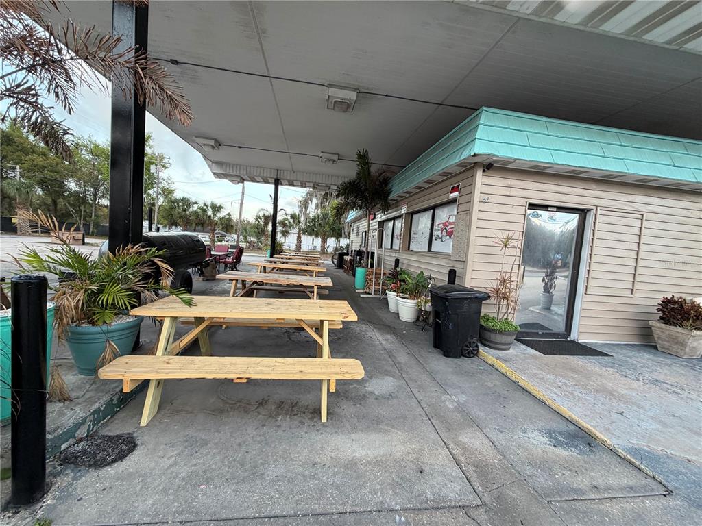 A covered outdoor patio features several wooden picnic tables and potted plants beside a building — 1095 US HIGHWAY 17 S, BARTOW, FL