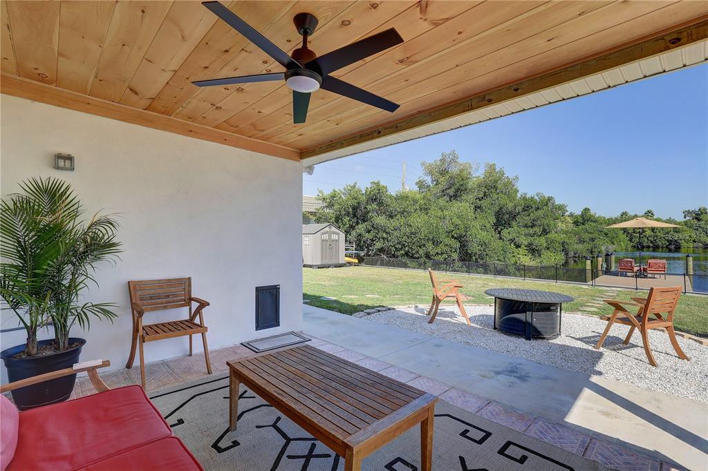 A covered patio with a wood ceiling and ceiling fan overlooks a backyard and canal — 265 96TH AVENUE N, ST PETERSBURG, FL