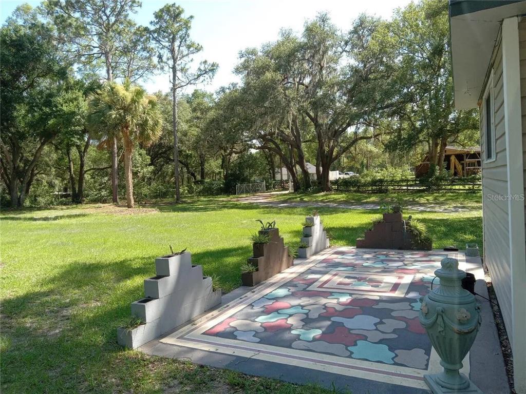 A view from a wooden deck looking out toward a sandy yard and large trees — 16395 SE 117TH AVENUE, WEIRSDALE, FL