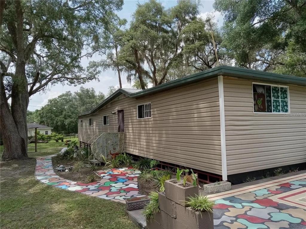 A patio with a patterned floor and tiered concrete planters sits beside a grassy yard — 16395 SE 117TH AVENUE, WEIRSDALE, FL