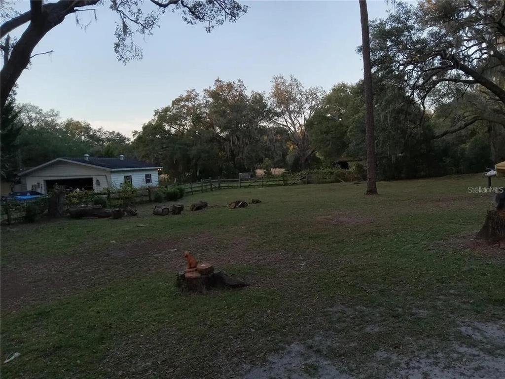 A grassy backyard features scattered tree stumps, a wooden fence, and a detached garage — 16395 SE 117TH AVENUE, WEIRSDALE, FL