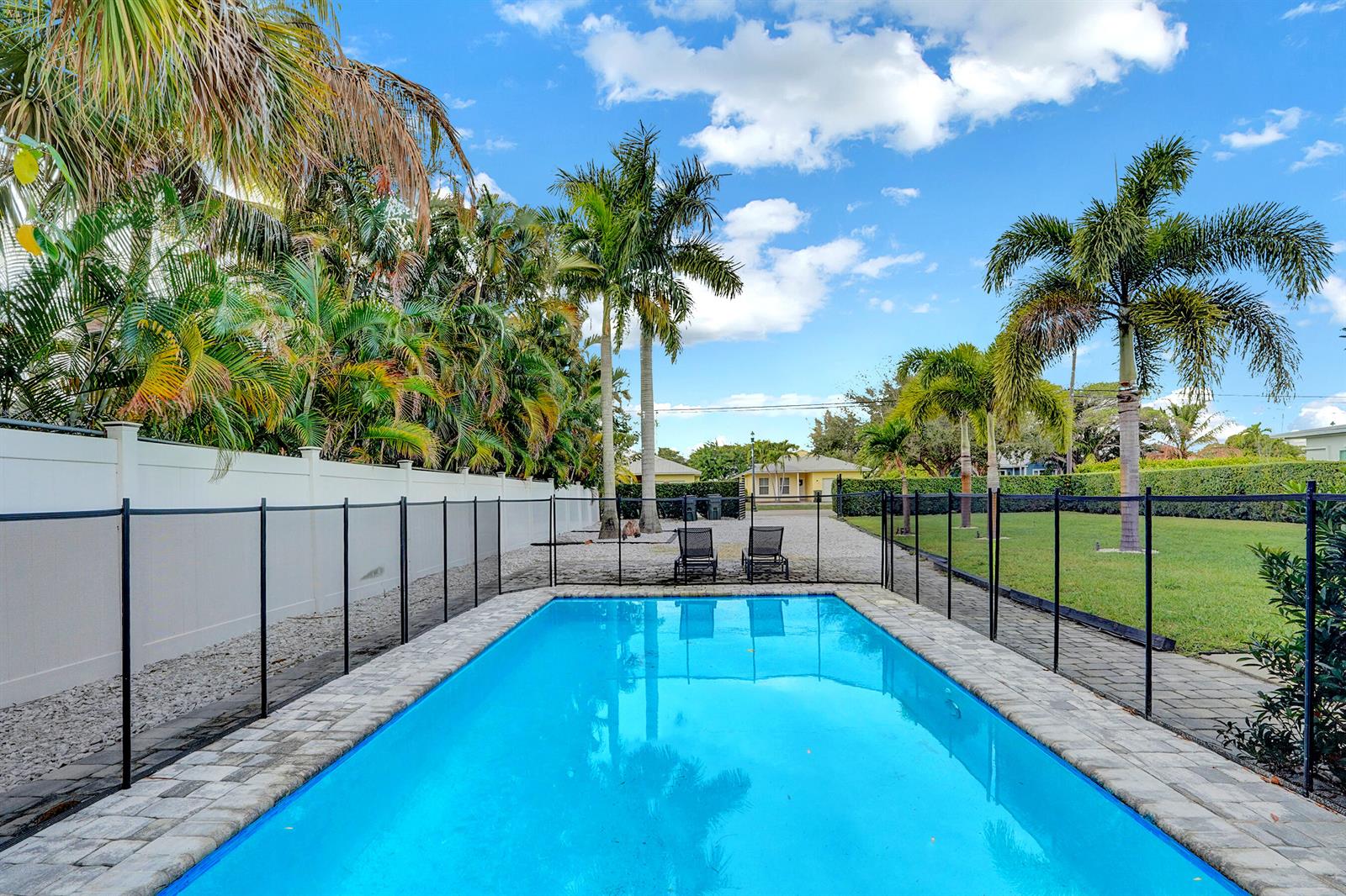 A rectangular swimming pool sits in a fenced backyard with palm trees and lounge chairs — 311 SE 3rd Avenue, Delray Beach FL 33483, DELRAY BEACH, FL