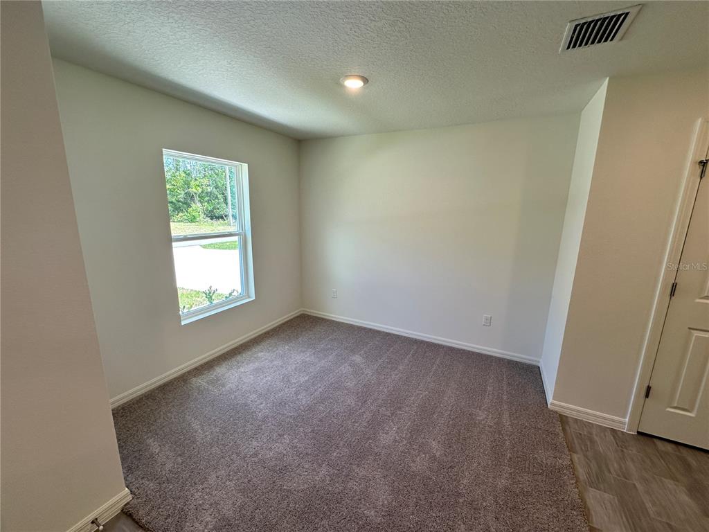 A small, empty room features beige carpet, white walls, a single window, and a door — 48 RIPPLING BROOK DRIVE, PALM COAST, FL