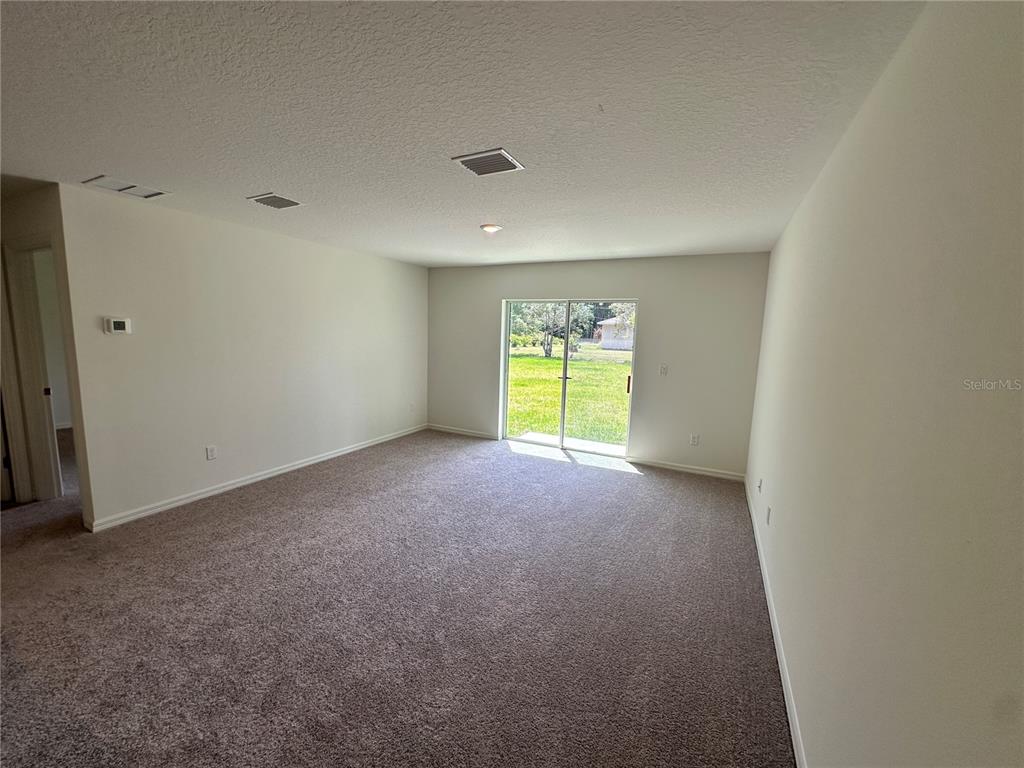 An empty room with beige carpet, white walls, and a sliding glass door to the backyard — 48 RIPPLING BROOK DRIVE, PALM COAST, FL