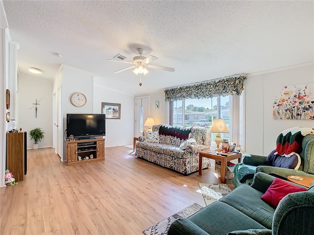 A living room features wood-look flooring, a ceiling fan, and a large window with valances — 157 ORANGEWOOD DRIVE, LAKE WALES, FL