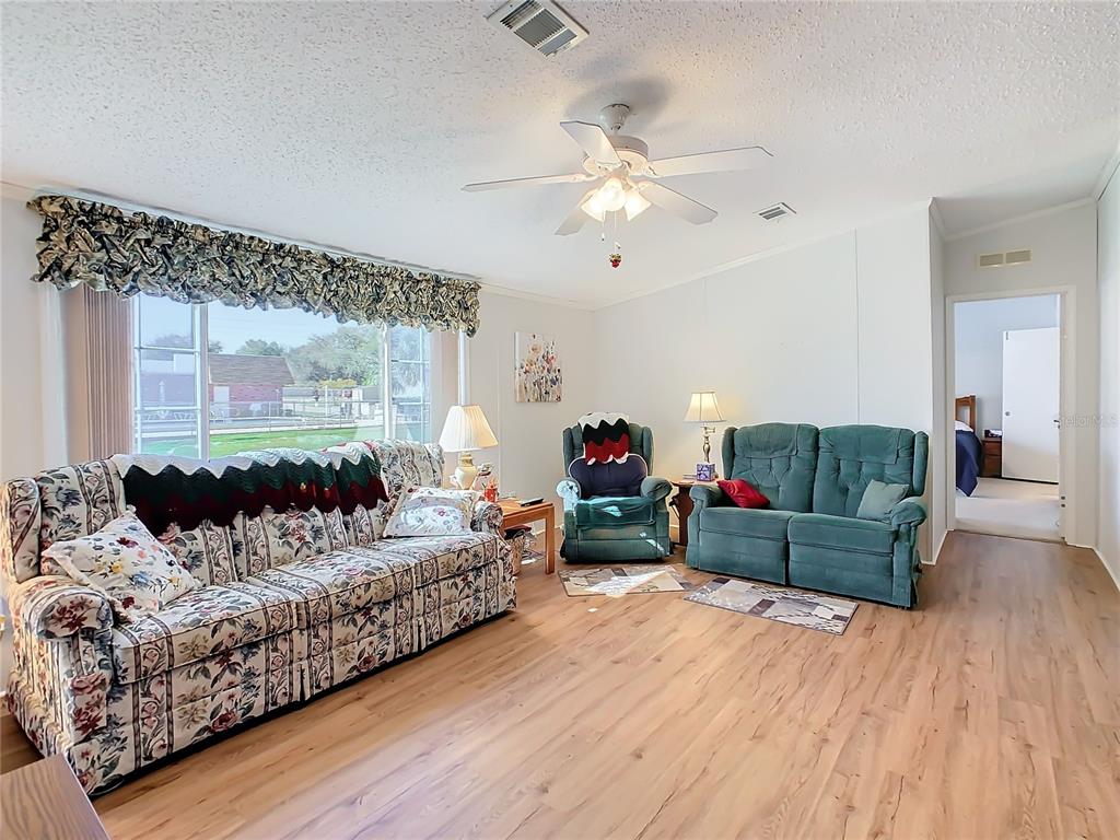 A living room features floral and green furniture, light wood-look flooring, and a ceiling fan — 157 ORANGEWOOD DRIVE, LAKE WALES, FL