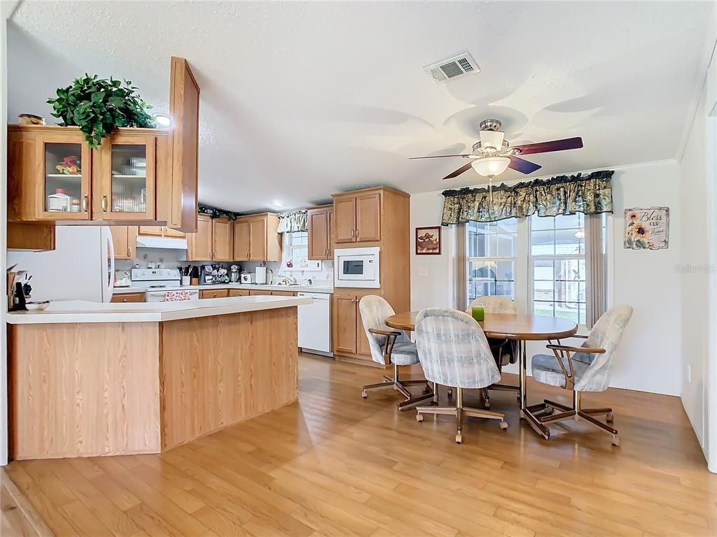 A kitchen and dining area with wood cabinets, light countertops, and a round wooden table — 157 ORANGEWOOD DRIVE, LAKE WALES, FL
