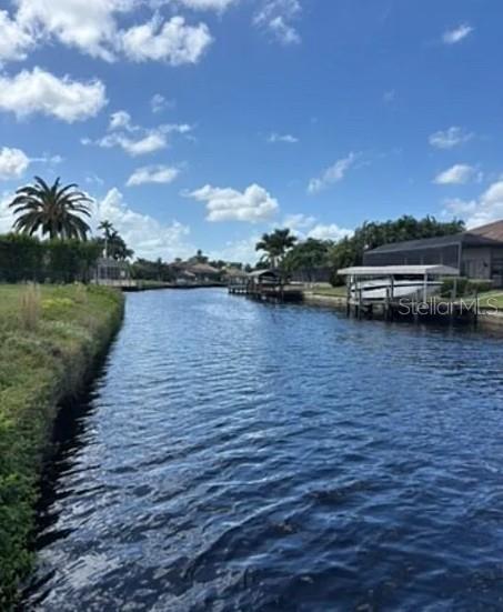 A canal view shows a grassy bank, boat docks, and palm trees under a blue sky — 2005 SE 20TH LANE, CAPE CORAL, FL