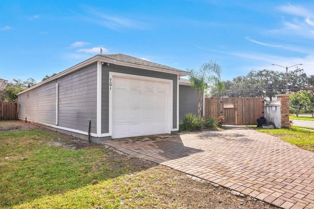 A detached gray garage with a white door and a brick paver driveway — 701 ASHLEY LANE, ORLANDO, FL