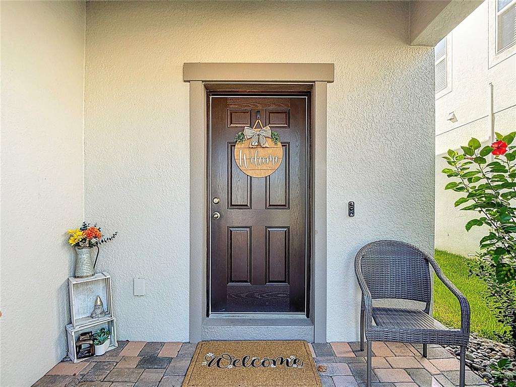 A dark brown front door with a welcome sign sits on a paved porch — 2960 AUTUMN ROCK DRIVE, ZEPHYRHILLS, FL