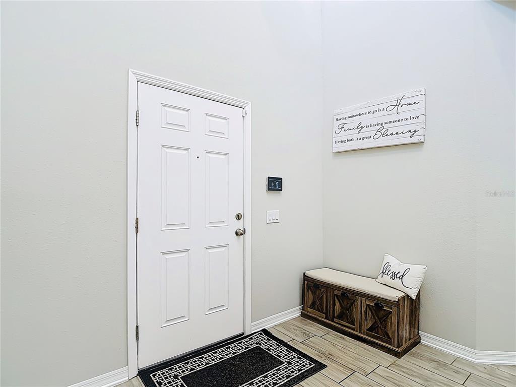 An entryway features a white front door, a wooden storage bench, and a wall sign — 2960 AUTUMN ROCK DRIVE, ZEPHYRHILLS, FL