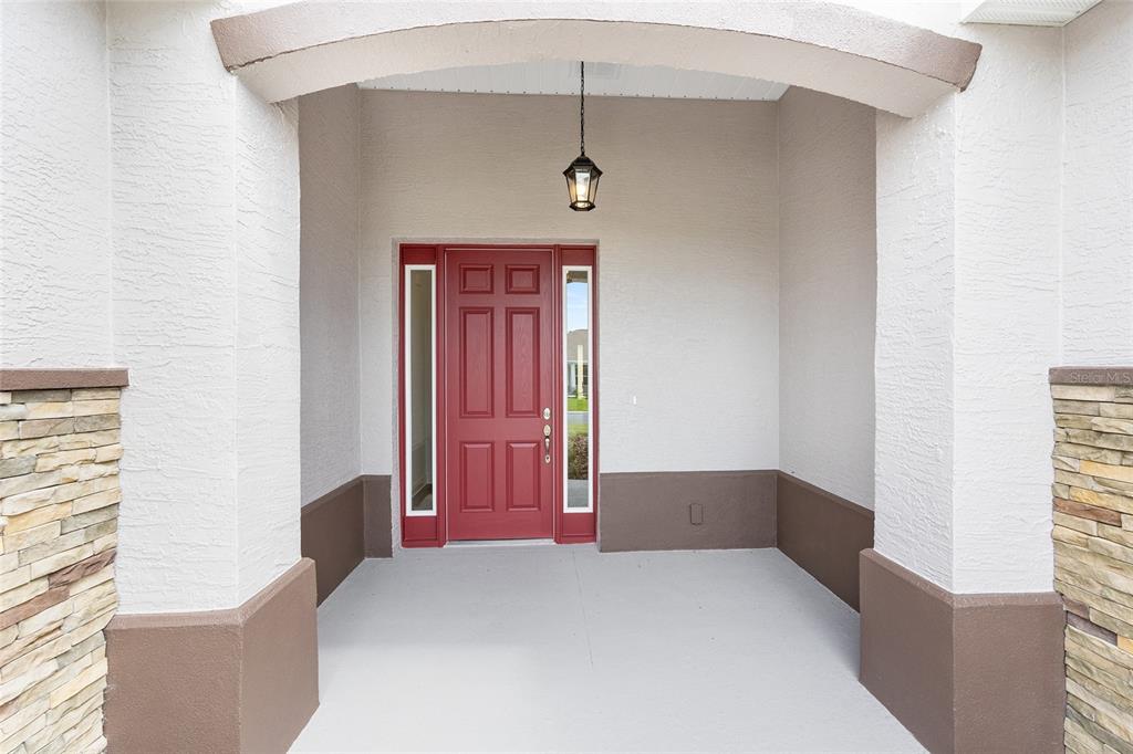 A covered entryway features a red front door with sidelights and stone-accented stucco columns — 10119 SW 106TH CIRCLE, OCALA, FL