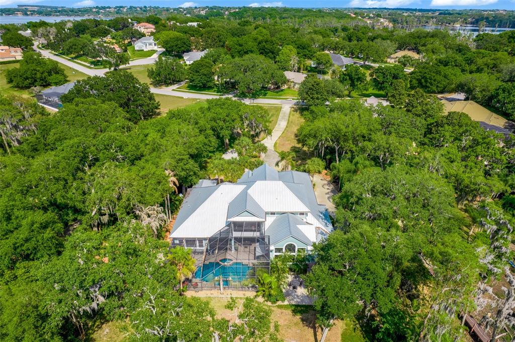 An aerial view shows a large house with a metal roof and a screened pool — 11610 OSPREY POINTE BOULEVARD, CLERMONT, FL