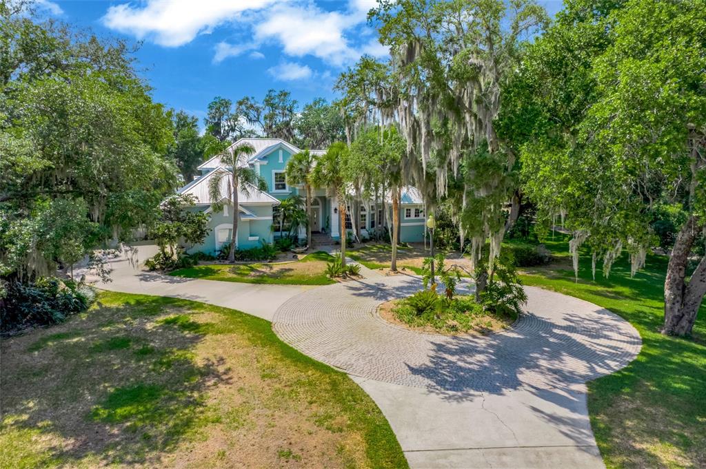 A two-story teal house with a circular brick driveway sits among mature trees — 11610 OSPREY POINTE BOULEVARD, CLERMONT, FL