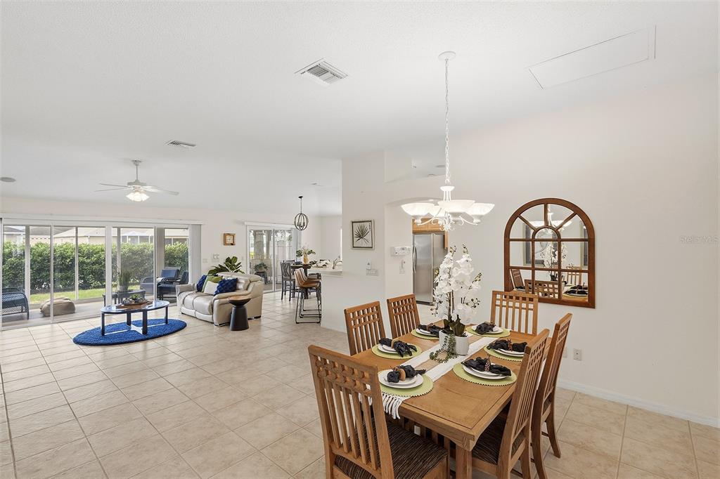 A dining area with a wooden table leads into an open-concept living room with tile floors — 1969 HAGOOD LOOP, THE VILLAGES, FL