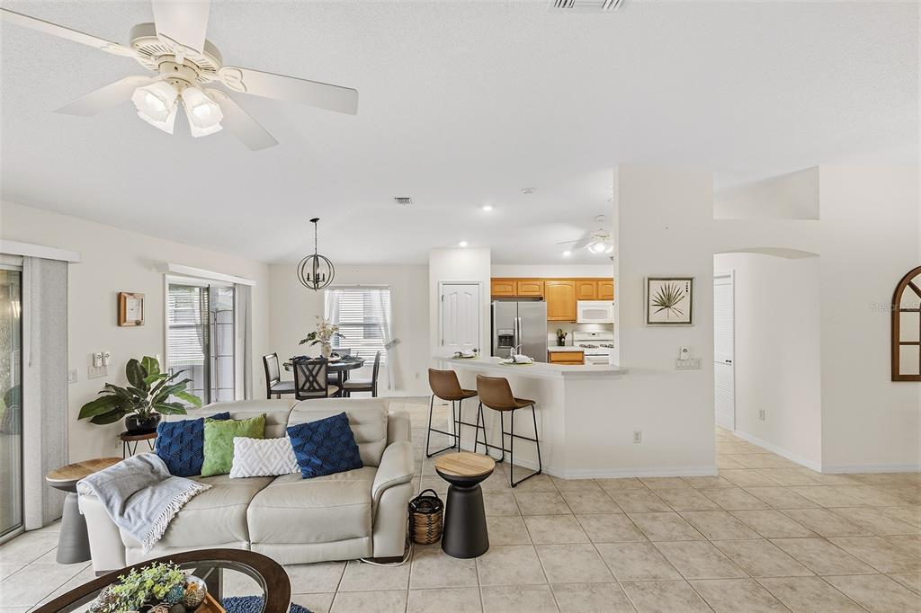 An open-concept living room and kitchen featuring tile flooring, a ceiling fan, and bar seating — 1969 HAGOOD LOOP, THE VILLAGES, FL