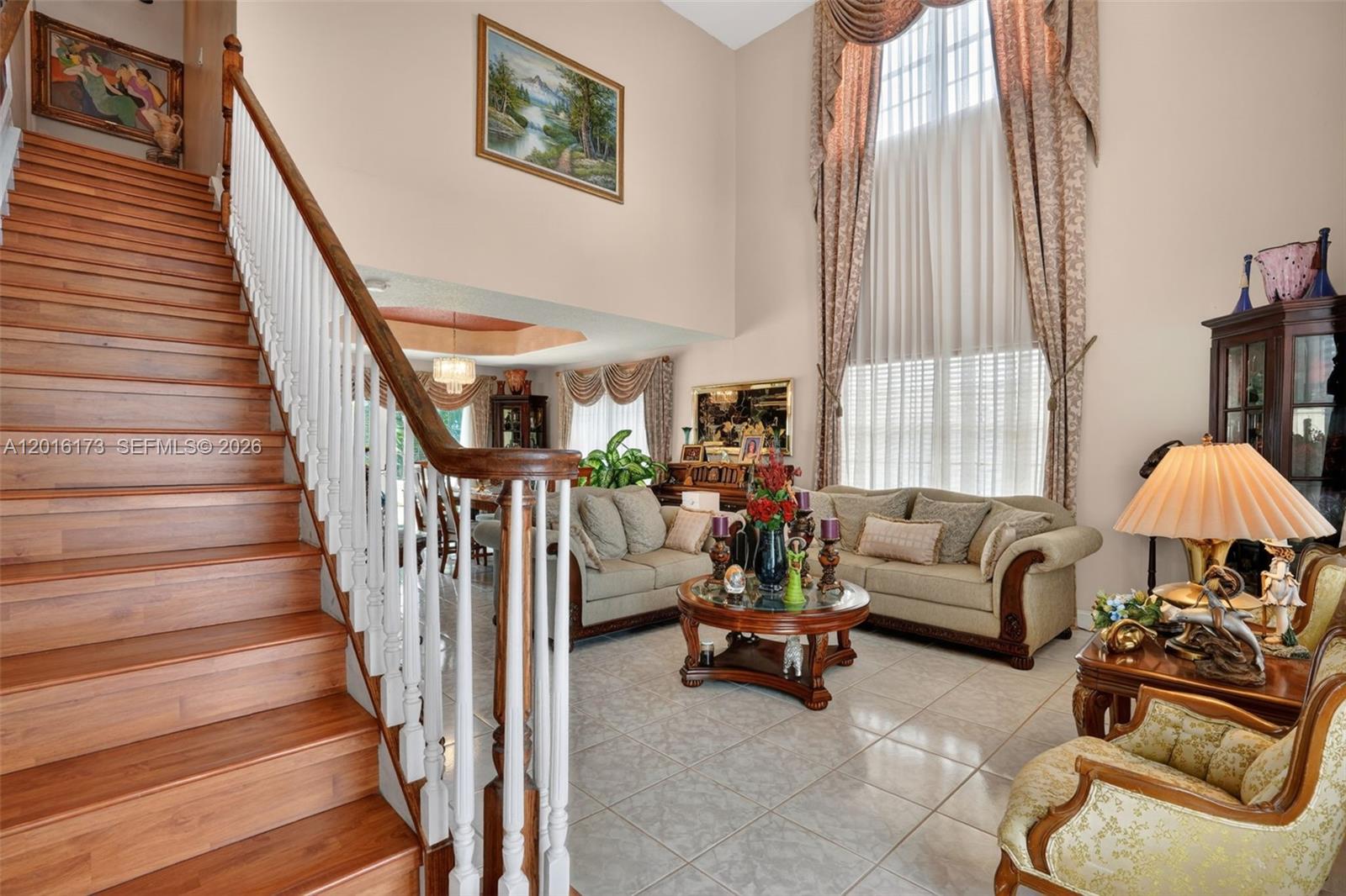 A living room with a wooden staircase, tile floors, and tall windows with draped curtains — 10331 SW 164th Ct, Miami FL 33196, MIAMI, FL