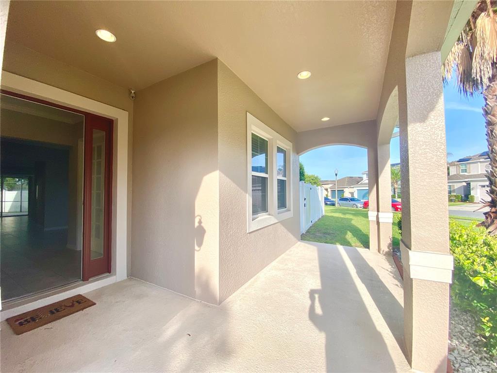 A covered concrete porch features recessed lighting, a red door, and a beige exterior wall — 1015 GRAND HILLTOP DRIVE, APOPKA, FL