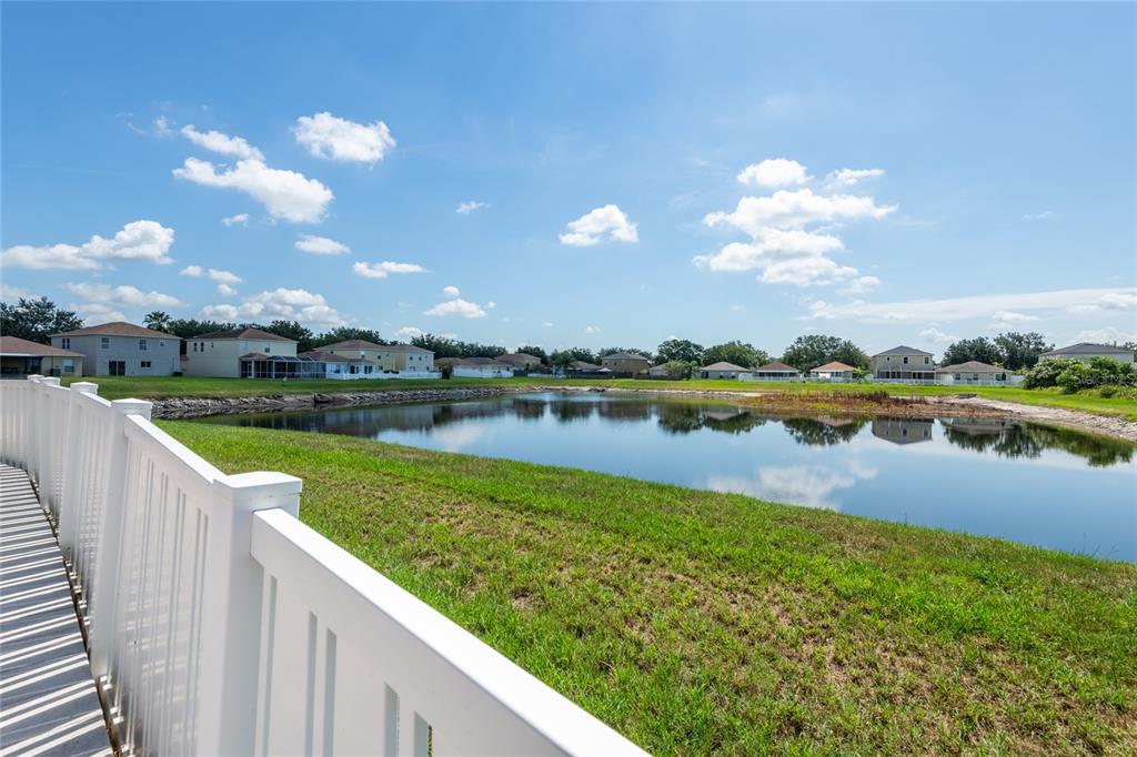 A white vinyl fence overlooks a pond surrounded by suburban houses under a blue sky — 10907 GOLDEN SILENCE DRIVE, RIVERVIEW, FL