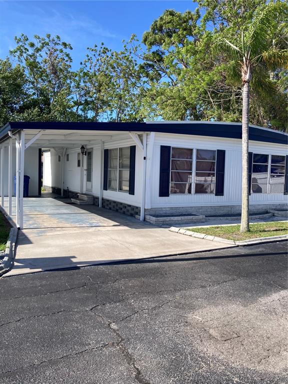 A white manufactured home with a carport and dark shutters sits beside a palm tree — 3212 W TIKI DRIVE, HOLIDAY, FL