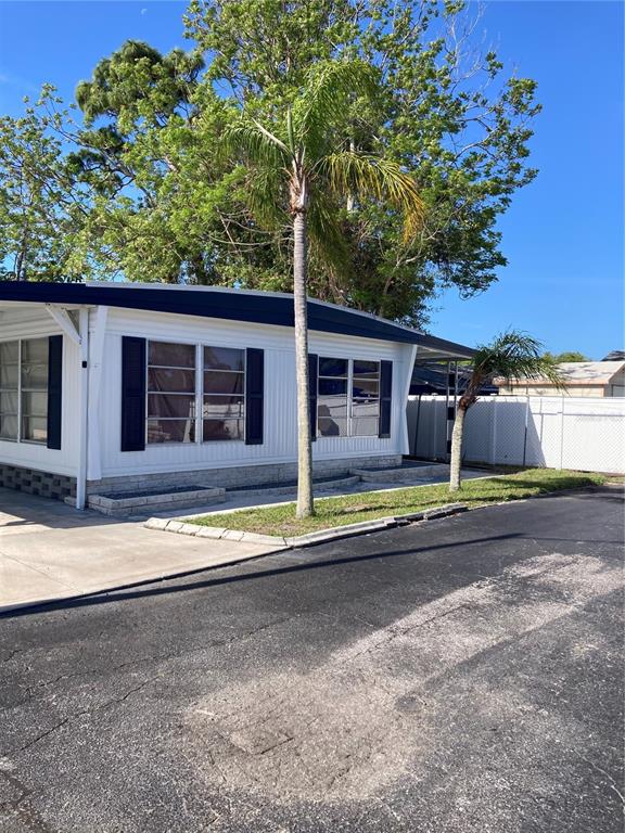 A white mobile home with dark shutters and a palm tree in the front yard — 3212 W TIKI DRIVE, HOLIDAY, FL