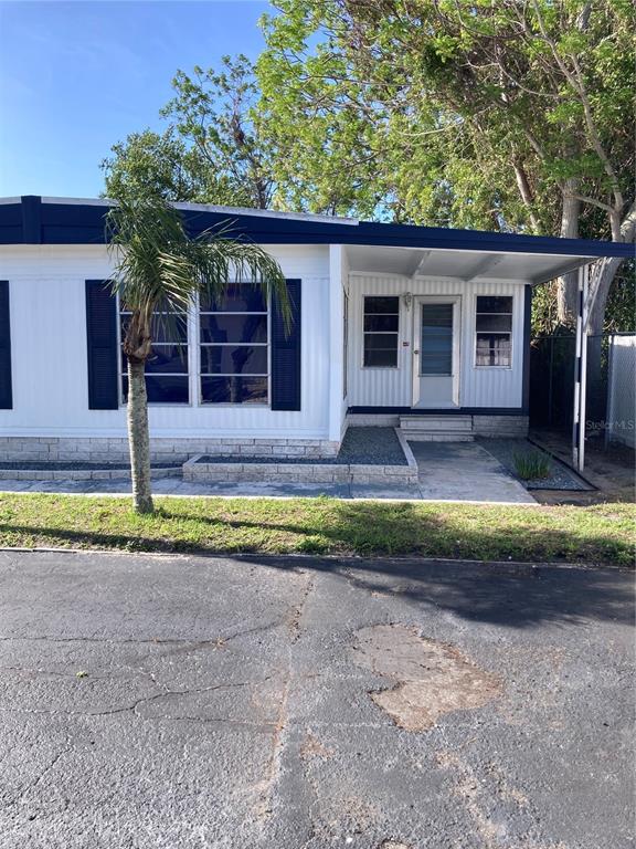 A single-story manufactured home features white siding, dark shutters, and a covered front entryway — 3212 W TIKI DRIVE, HOLIDAY, FL