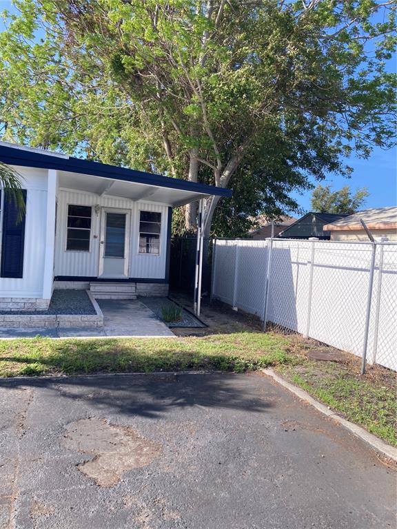 The exterior of a mobile home features a covered porch, white siding, and a chain-link fence — 3212 W TIKI DRIVE, HOLIDAY, FL