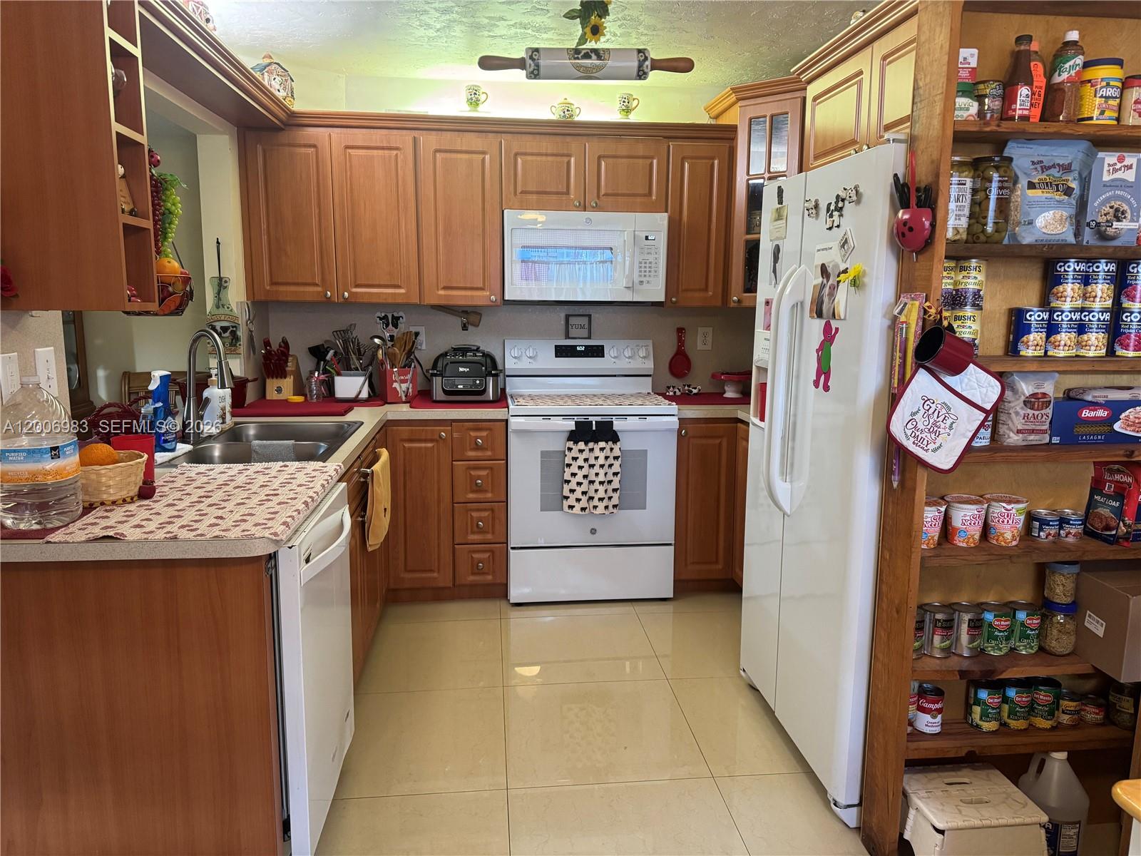 A kitchen features wood cabinets, white appliances, tile flooring, and an open pantry shelf — 471 NE 210TH CIRCLE TER # 103, Miami FL 33179, MIAMI, FL