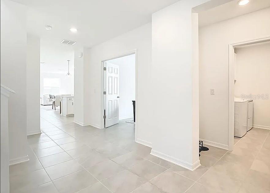 A bright hallway with light tile flooring leads to an open kitchen and laundry room — 16863 FIESTA DRIVE, PORT CHARLOTTE, FL