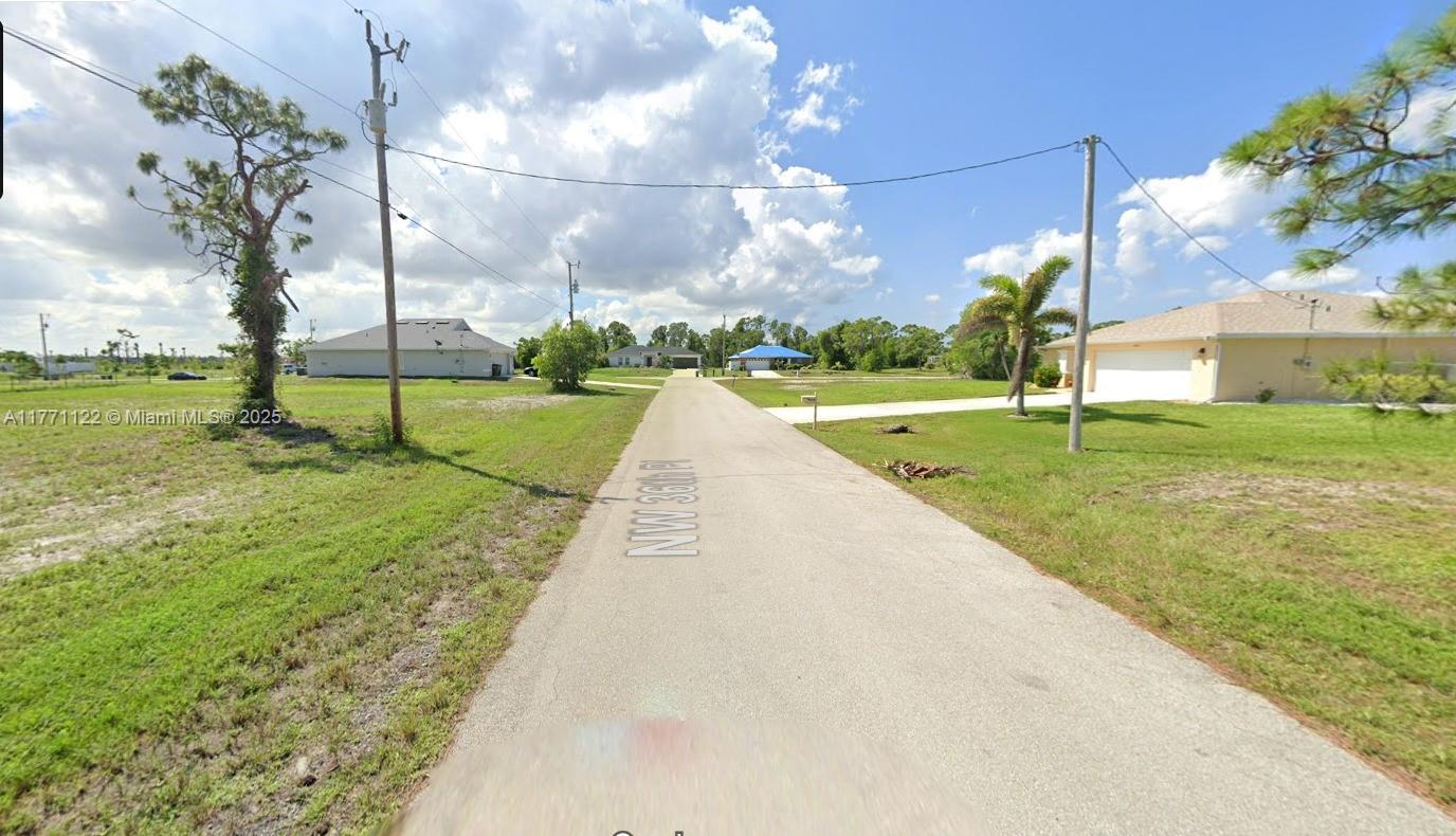 A paved road stretches between grassy lots with houses and utility poles under a cloudy sky — 4309 NW 36 th PL, Cape Coral FL 33993, CAPE CORAL, FL