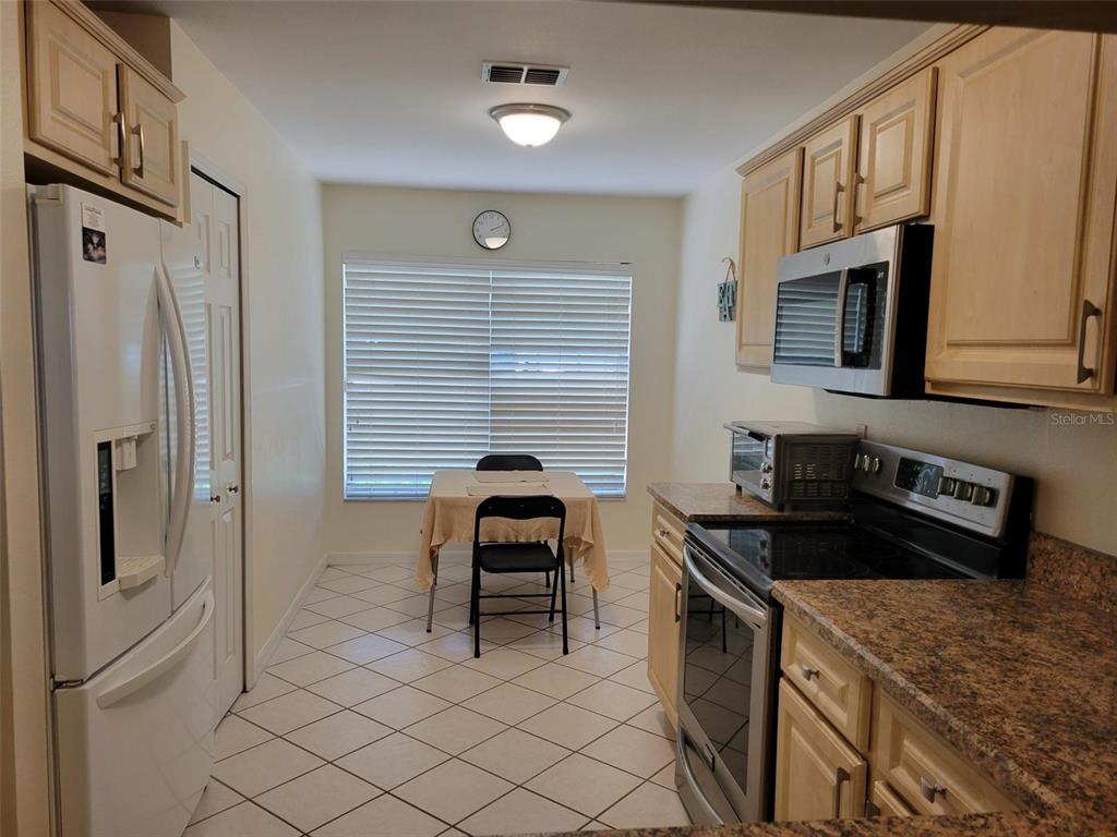 A kitchen with light wood cabinets, granite countertops, stainless steel appliances, and a dining area — 2160 ADDISON AVENUE, CLERMONT, FL